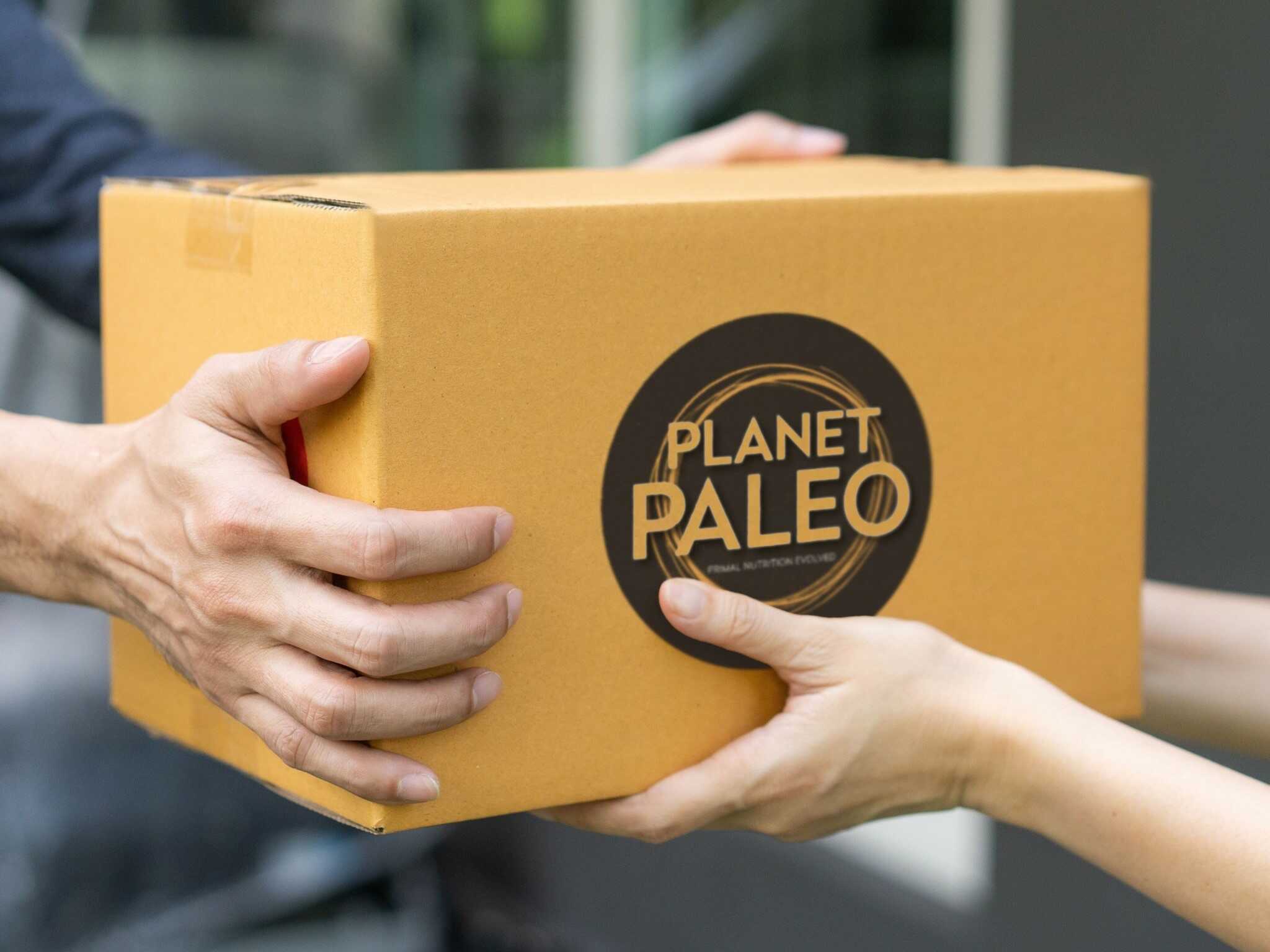 Hands passing a cardboard box with a large circular Planet Paleo logo on the front.